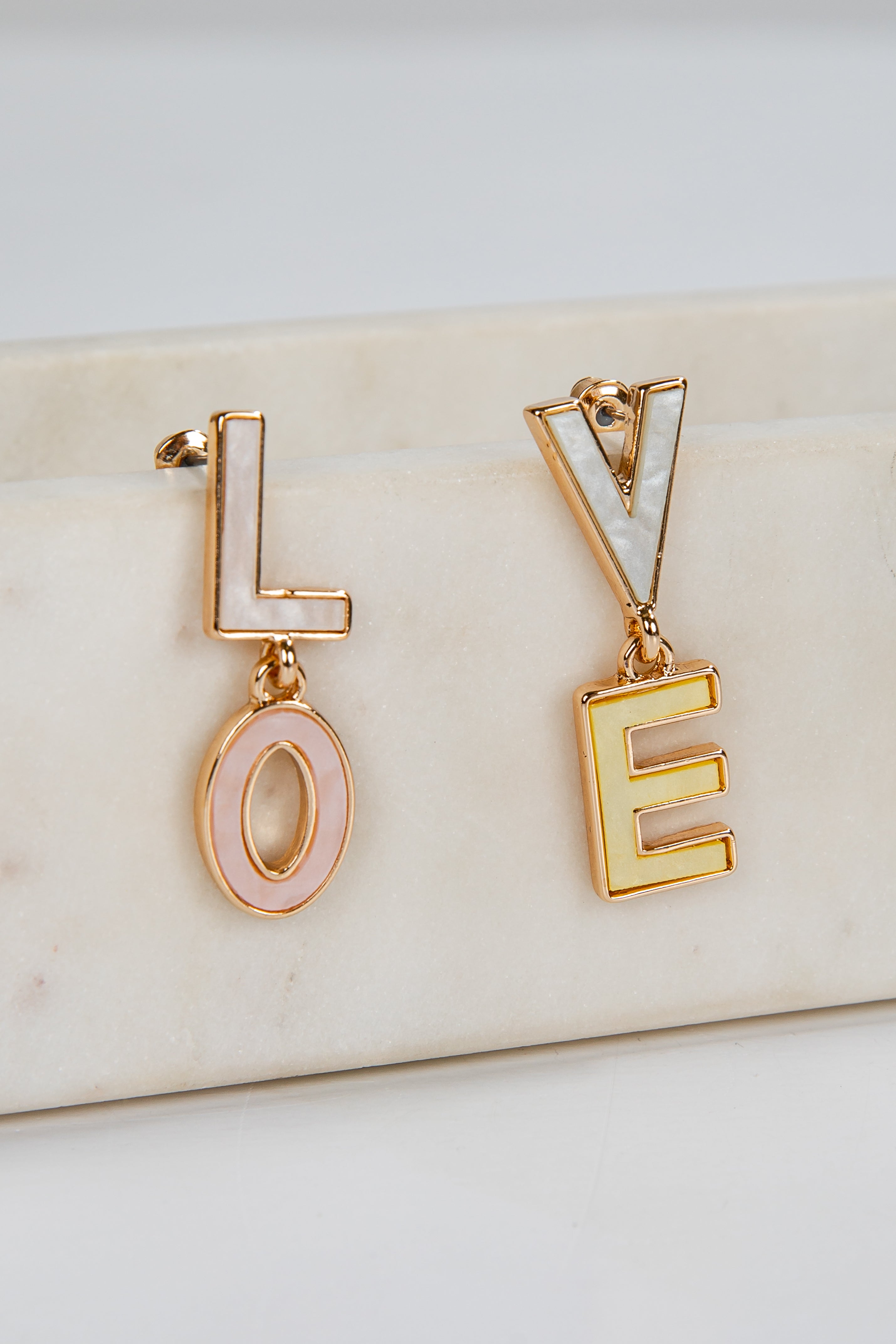 Gold earrings spelling 'LOVE' on a marble surface