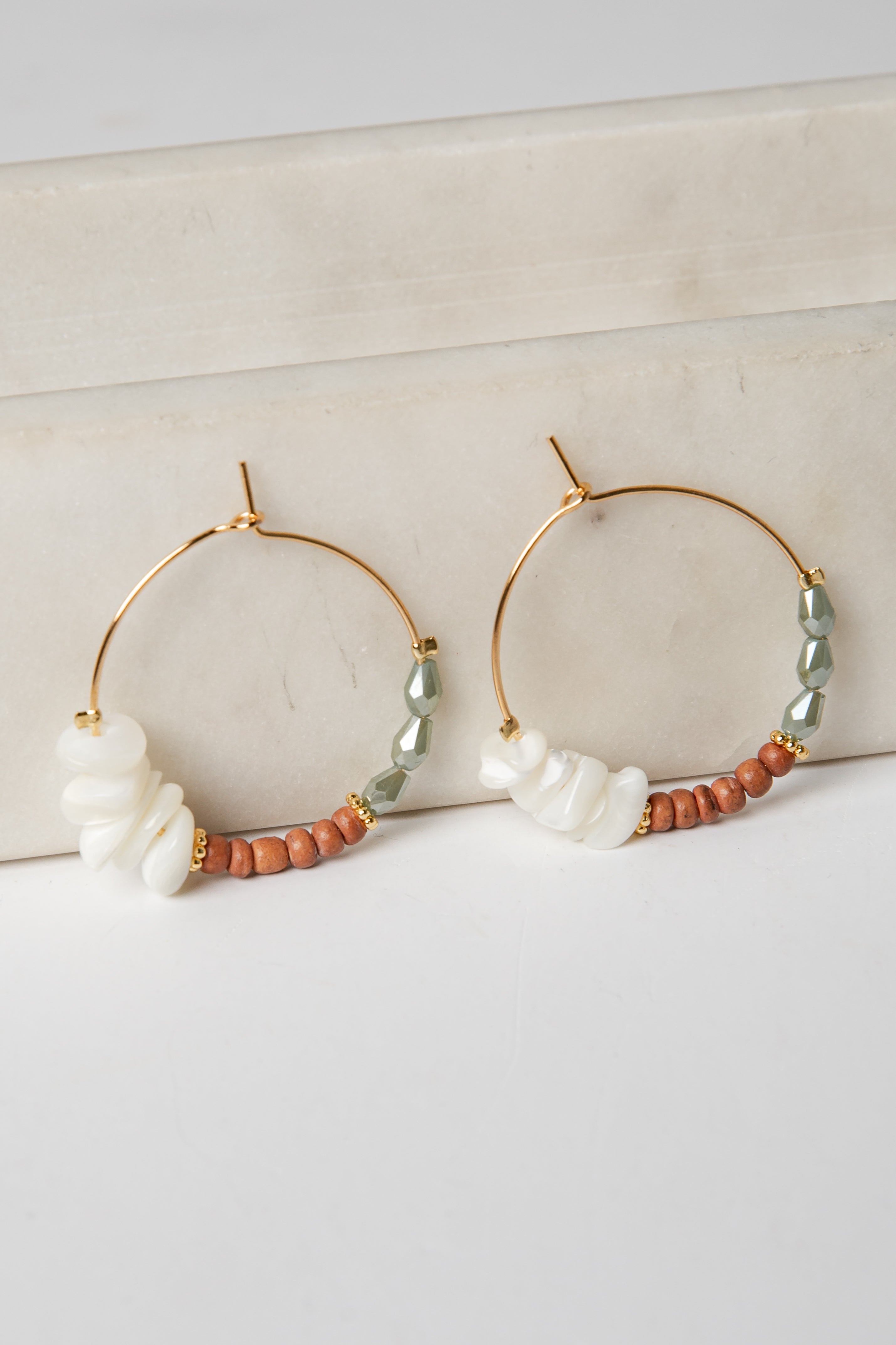 Gold hoop earrings with pearls and beads on a light background