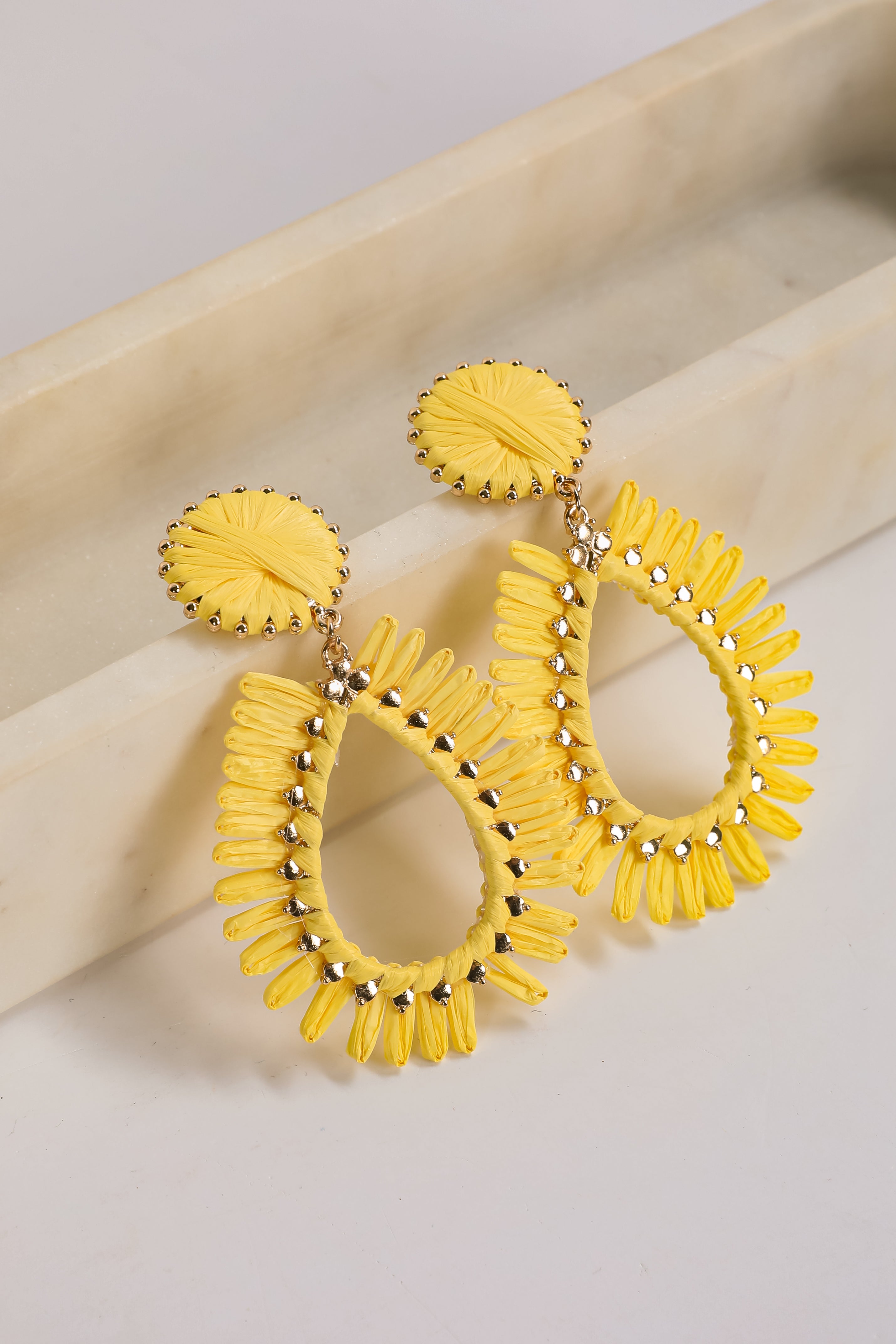 Yellow earrings with intricate designs on a beige surface