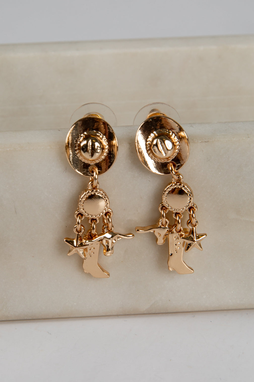 Gold earrings with star and figure charms on a beige surface
