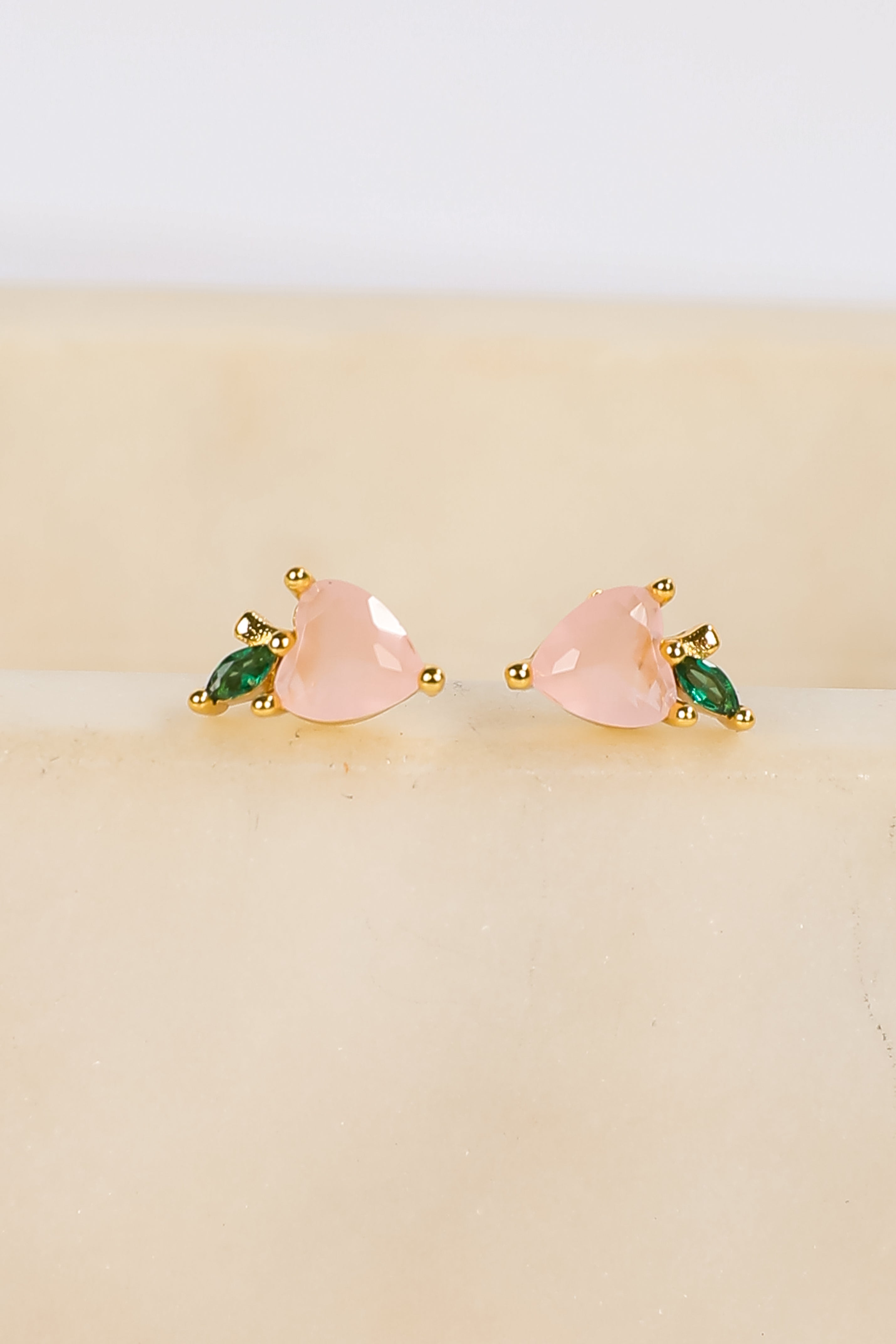 Pair of earrings with pink and green stones on a beige background