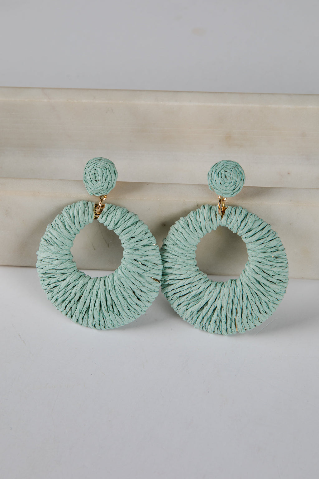 Pair of light blue hoop earrings on a white surface with a beige background