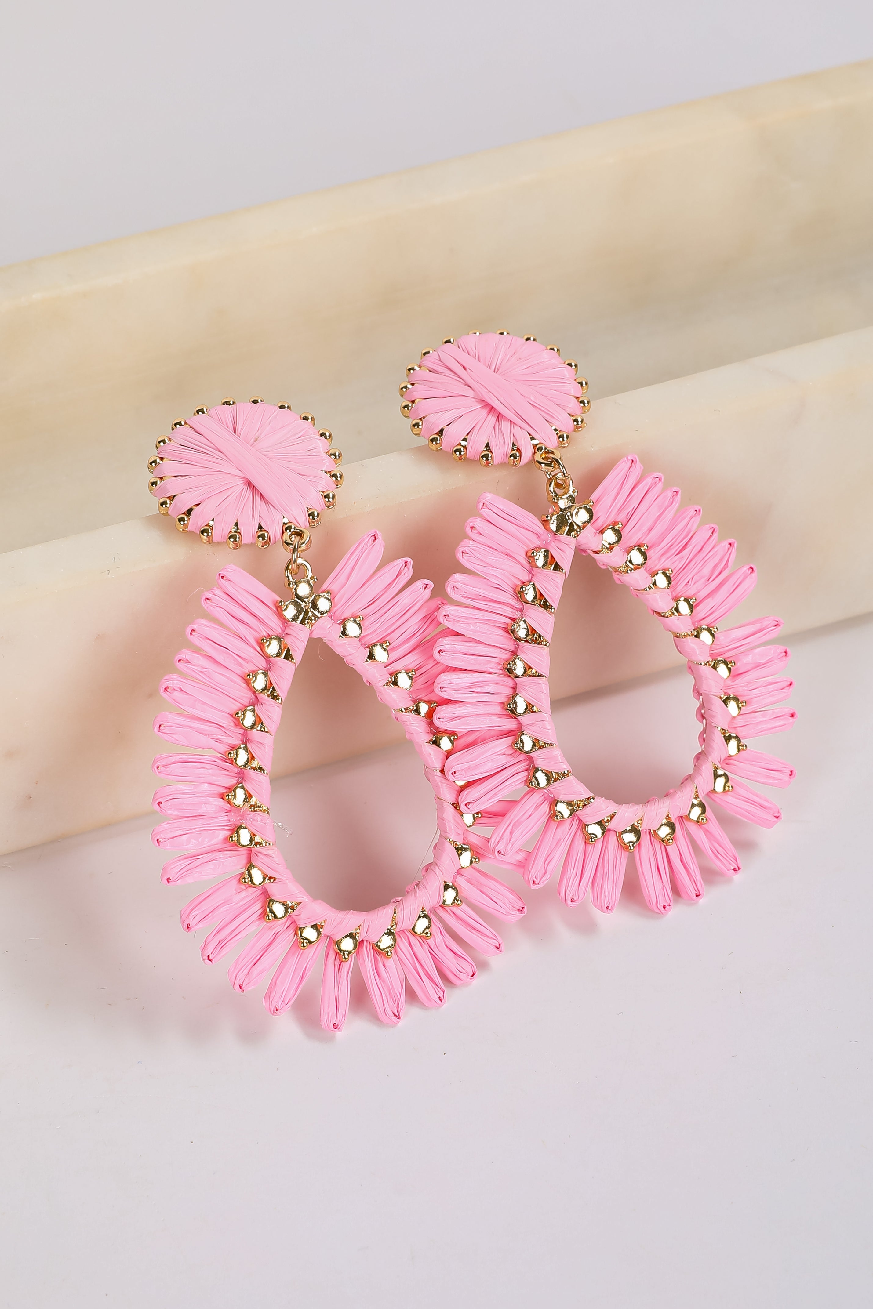 Pink hoop earrings with gold accents on a beige surface